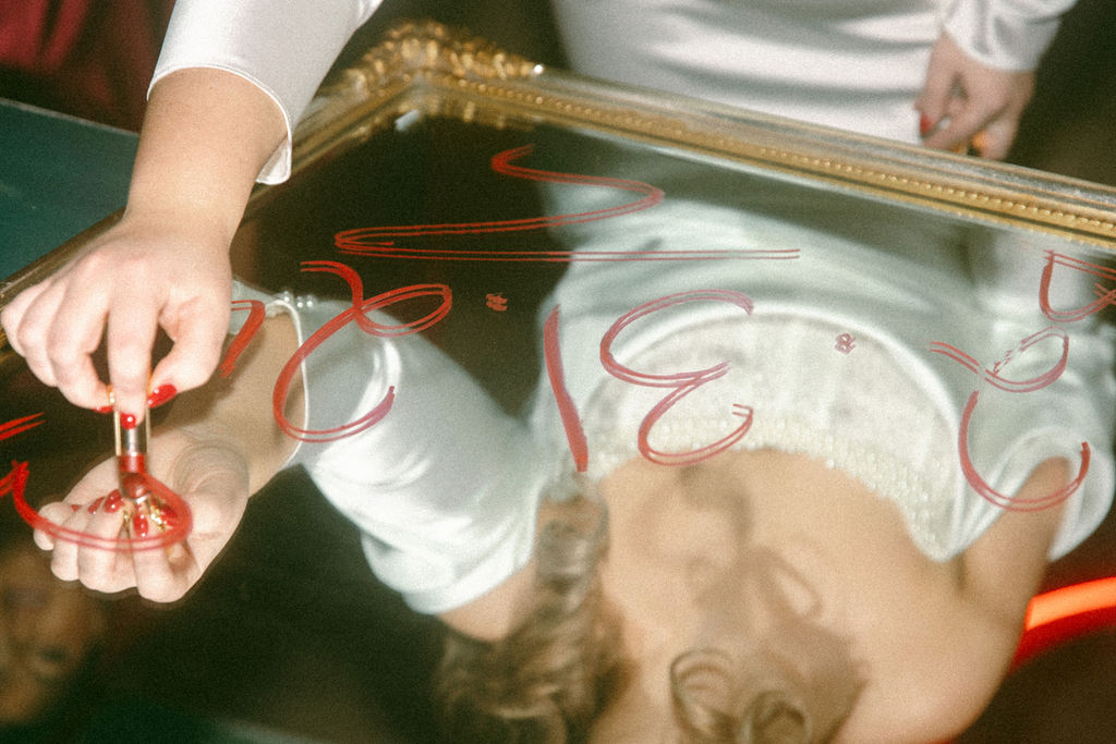 A bride writes her wedding date on a mirror with red lipstick in a photo taken at her Philadelphia wedding 