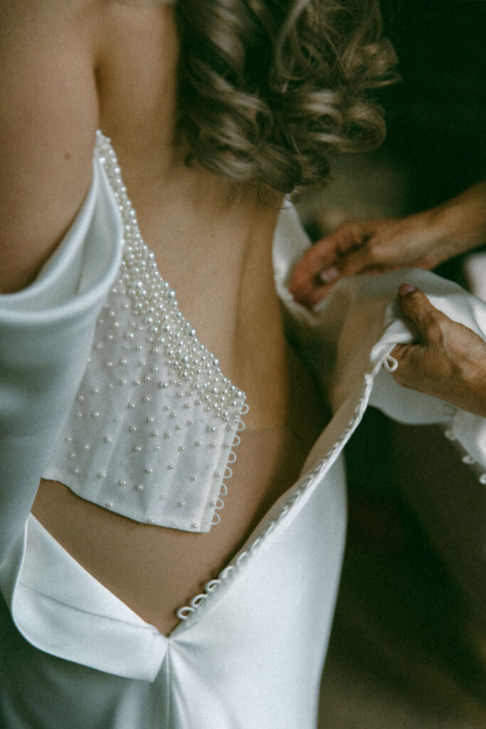 A bride is buttoned into her dress before her her Philadelphia wedding at La Chinesca
