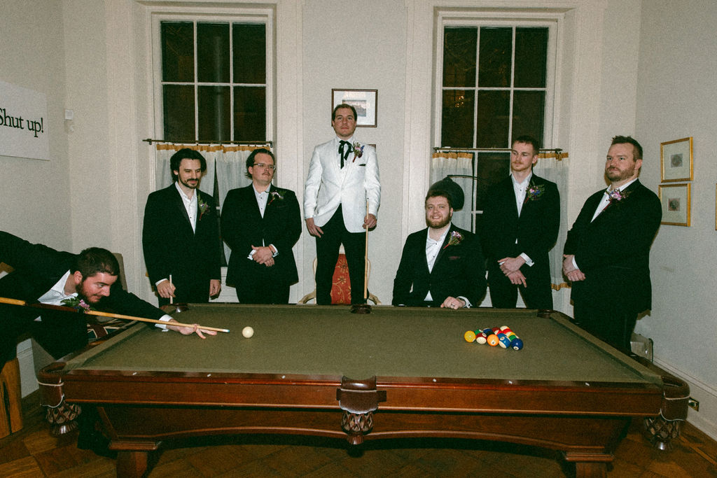 A groom in a white tux is photographed playing pool with his groomsmen at a unique wedding venue philadelphia