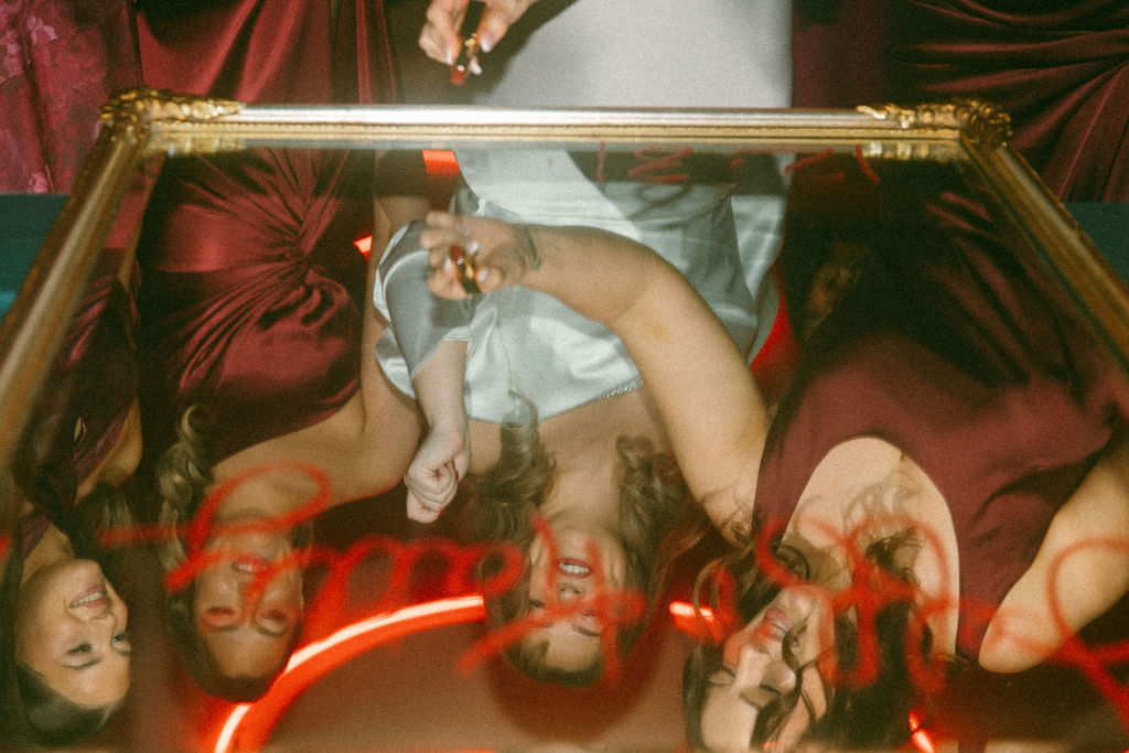 A bride & her bridesmaids smile into a mirror at her La Chinesca Philly wedding 