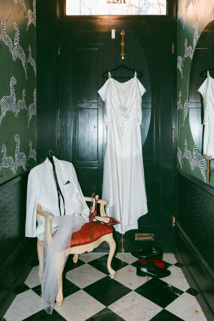 A wedding gown hangs from a black velvet hanger next to a groom's suit in a room at La Chinesca Philly 