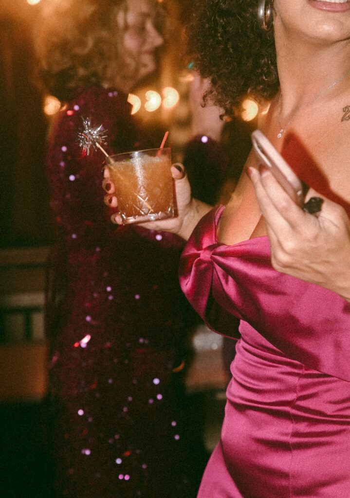 A wedding guest in a wine colored satin gown holds a cocktail at a NYE Philadelphia wedding  