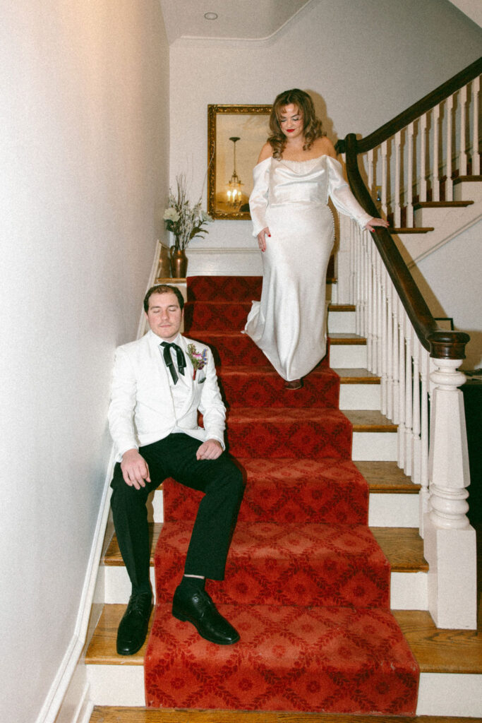A bride in a satin gown walks down the staircase for a first look with her groom at their Philadelphia wedding 