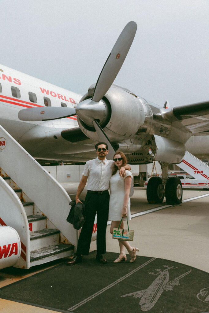 A bride and groom posing in front of the vintage Connie airplane cocktail lounge at the TWA Hotel wedding venue