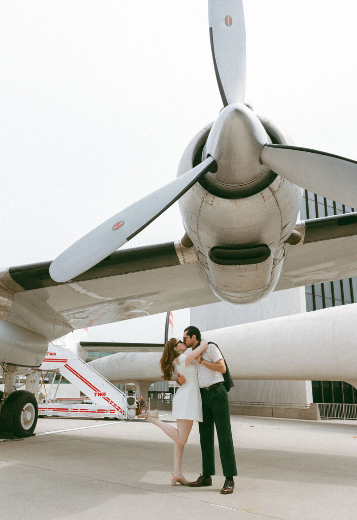 A bride and groom posing in front of the vintage Connie airplane cocktail lounge at the TWA Hotel wedding venue
