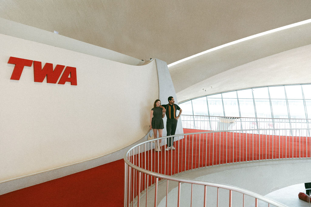 Couple wearing 1960's clothing posed with the sweeping architecture of the TWA Hotel